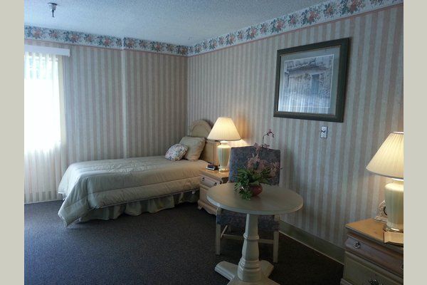 Senior living bedroom interior at Lakewood Gardens with bed, desk, art decor, and accessories.