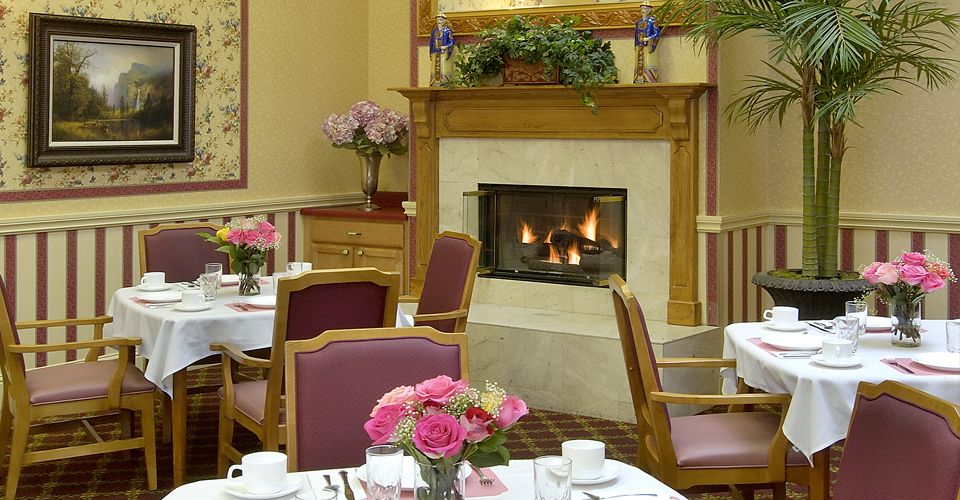 Senior residents dining in El Cerrito Royale's elegant dining room with fireplace and floral decor.