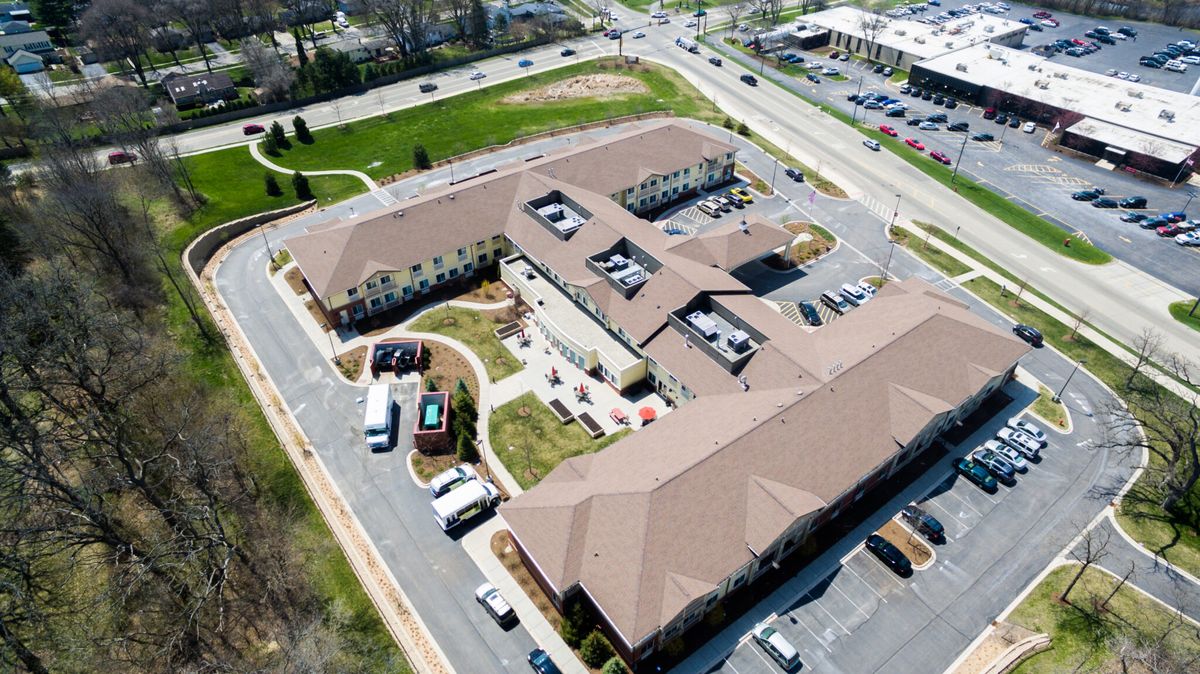 Aerial view of Three Oaks Assisted Living and Memory Care community with buildings, houses, and cars.
