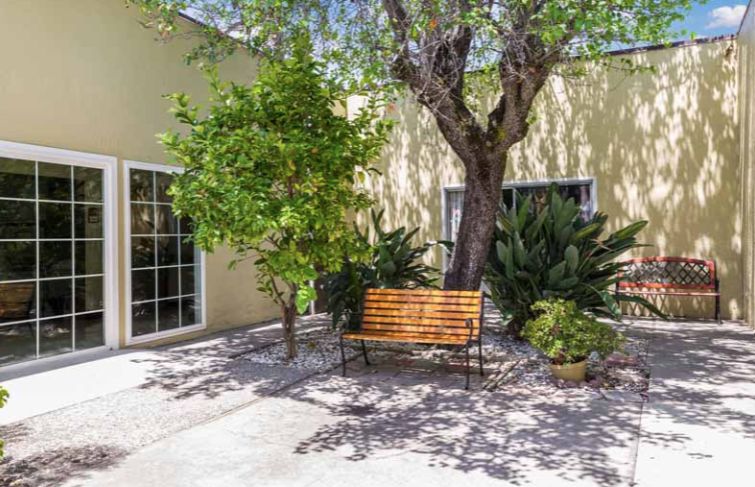 Senior living villa at Excell Health Care Center with lush backyard, oak trees, and cozy patio.
