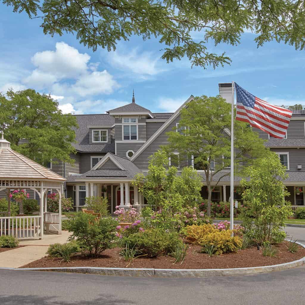 Outdoors view of Goddard House senior living community in a suburban neighborhood with American flag.