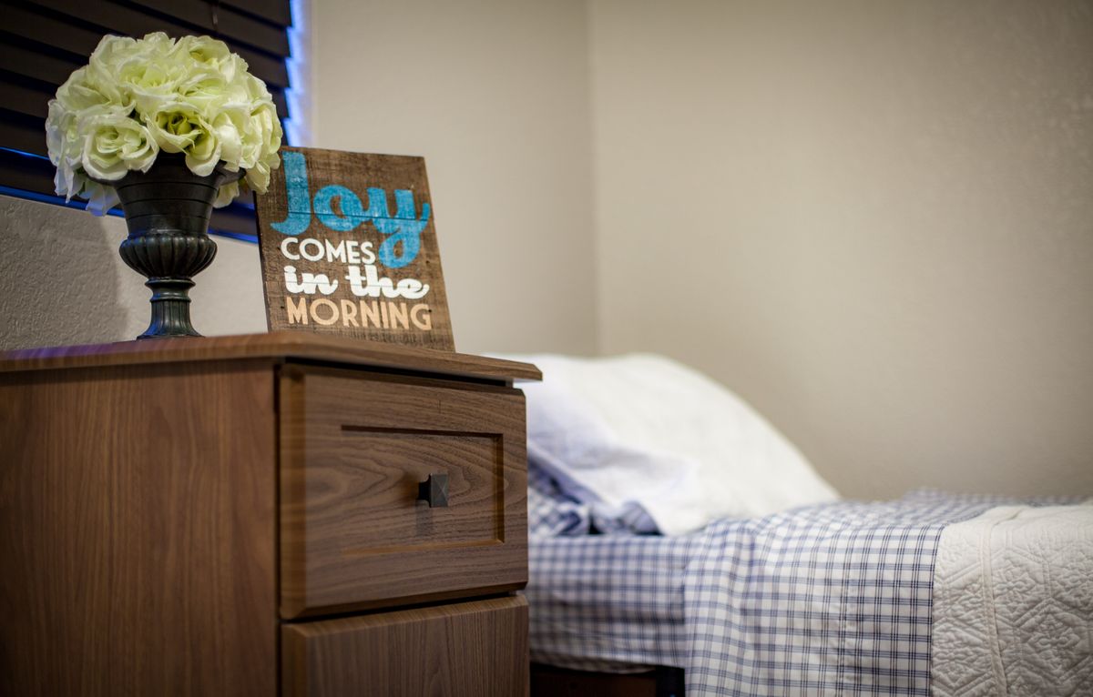 Senior living community bedroom with flower arrangements, wooden furniture, and a laptop.