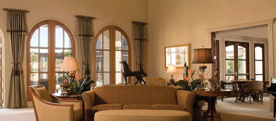 Senior living room interior at Oakmont of Segovia with French windows, furniture, and horse decor.