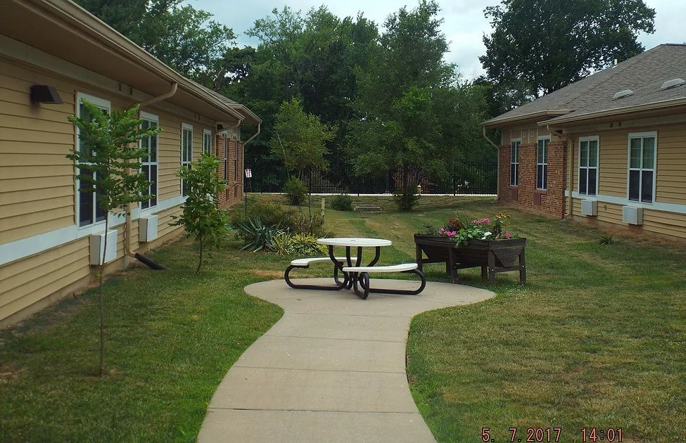 Backyard view of Christian Care Home, featuring lush greenery, patio furniture, and urban architecture.