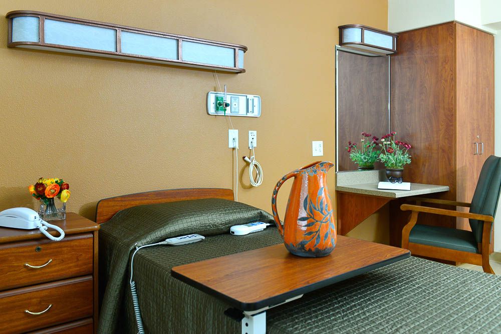 Interior view of Villa Manor Care Center featuring a well-designed bedroom with wooden furniture and plants.