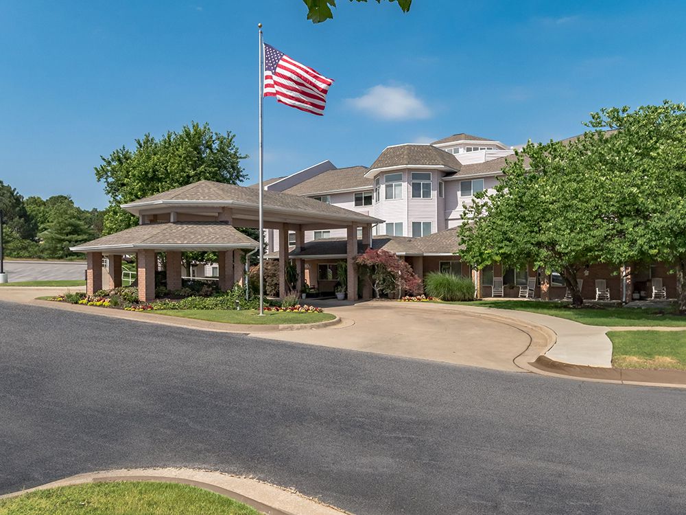 City suburban senior living community, Gardens At Arkanshire, with lush greenery and flag.