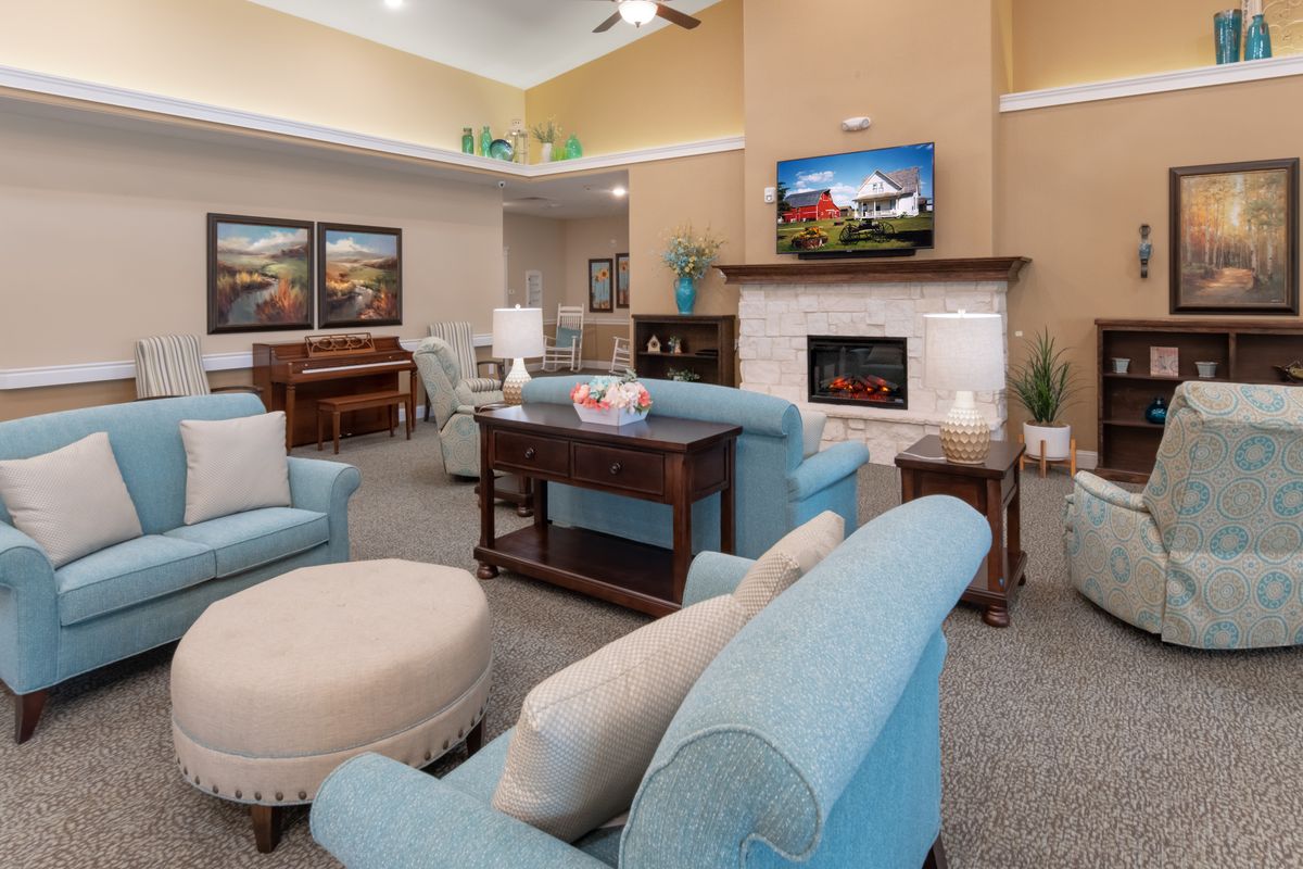 Senior living community interior with piano, TV, fireplace, and art in a cozy living room setting.