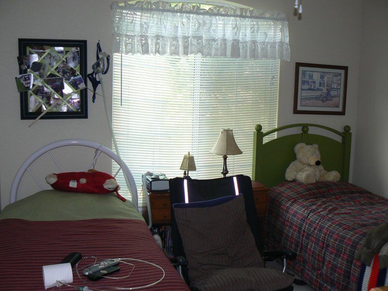Senior resident in a furnished dorm room at Guardian Angel Home Care II with decor and electronics.
