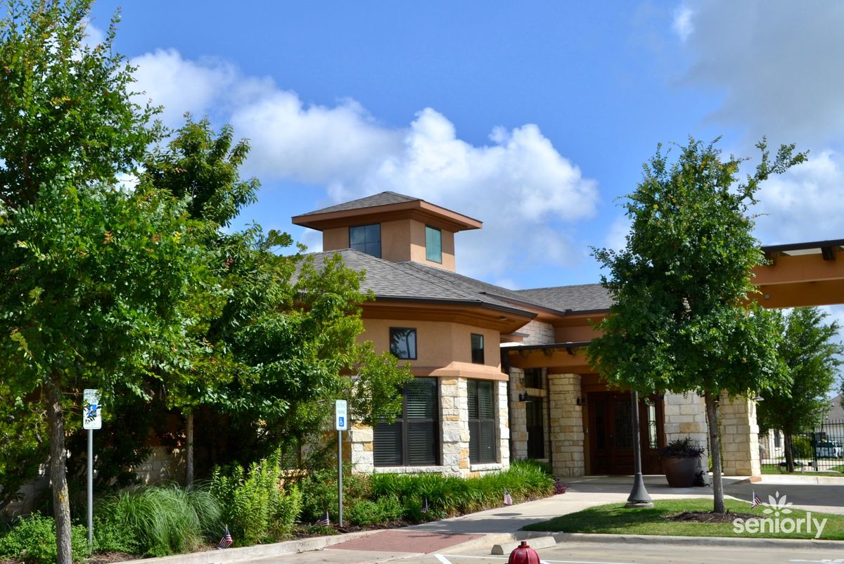 Summer view of Auberge At Onion Creek senior living community with lush vegetation and oak trees.