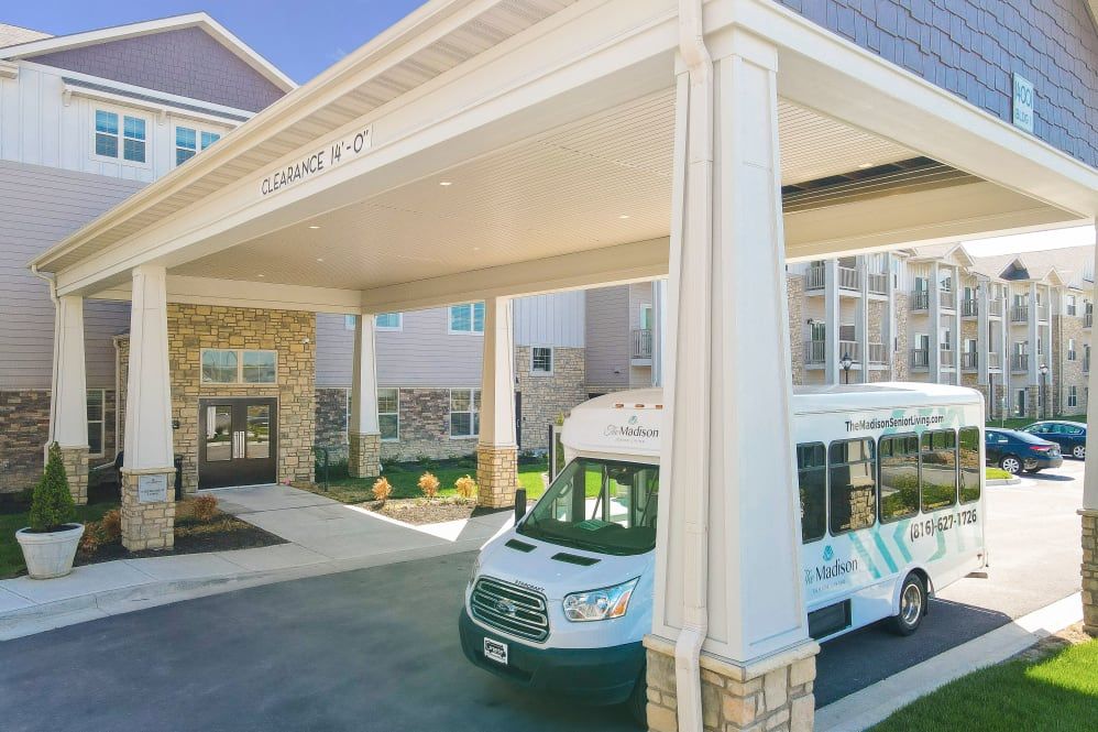 Plant-filled portico of The Wellington Senior Living building with a bus for resident transportation.