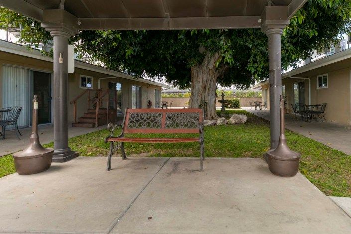 Senior living community, Rose Villa Healthcare Center, featuring a bench, porch, and patio amidst nature.