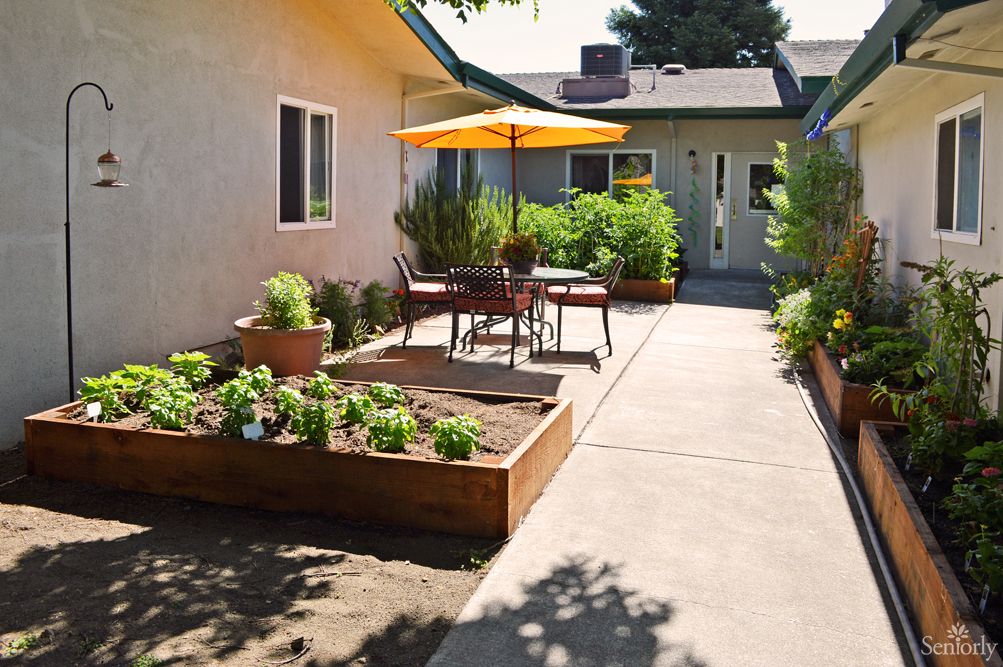 Pathway in Primrose Alzheimer's Living community with garden, patio furniture, and potted plants.