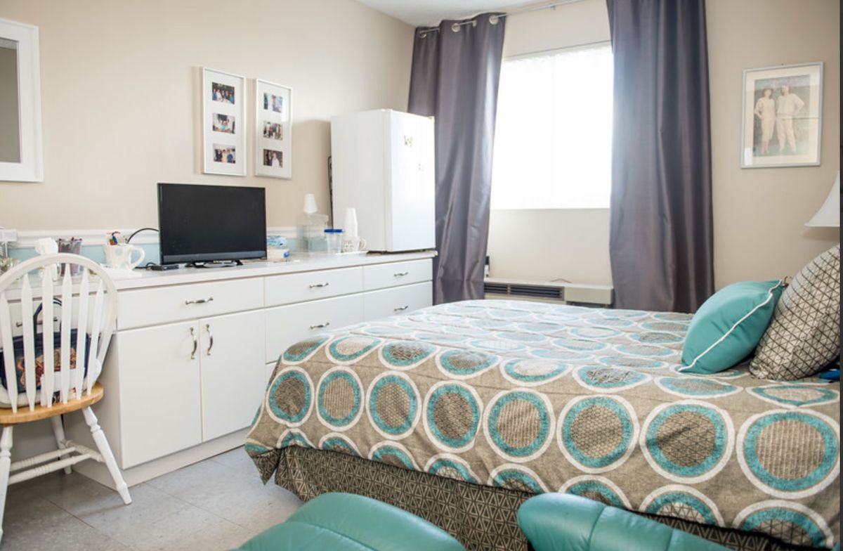 Senior living community bedroom with modern decor, furniture, electronics, and resident at Residential Plaza at Blue Lagoon.