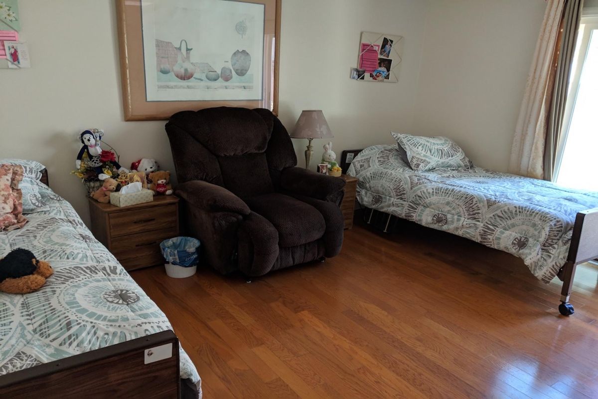 Senior resident in a furnished bedroom at Angel Genesis Guest Home with hardwood flooring.