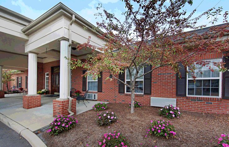 Architectural view of Downriver Estates Senior Living community featuring houses, portico, plants, and furniture.