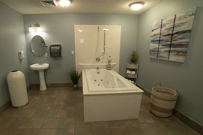 Senior resident in a well-designed bathroom at Brookdale Lenoir, featuring a tub, sink, and indoor plant.