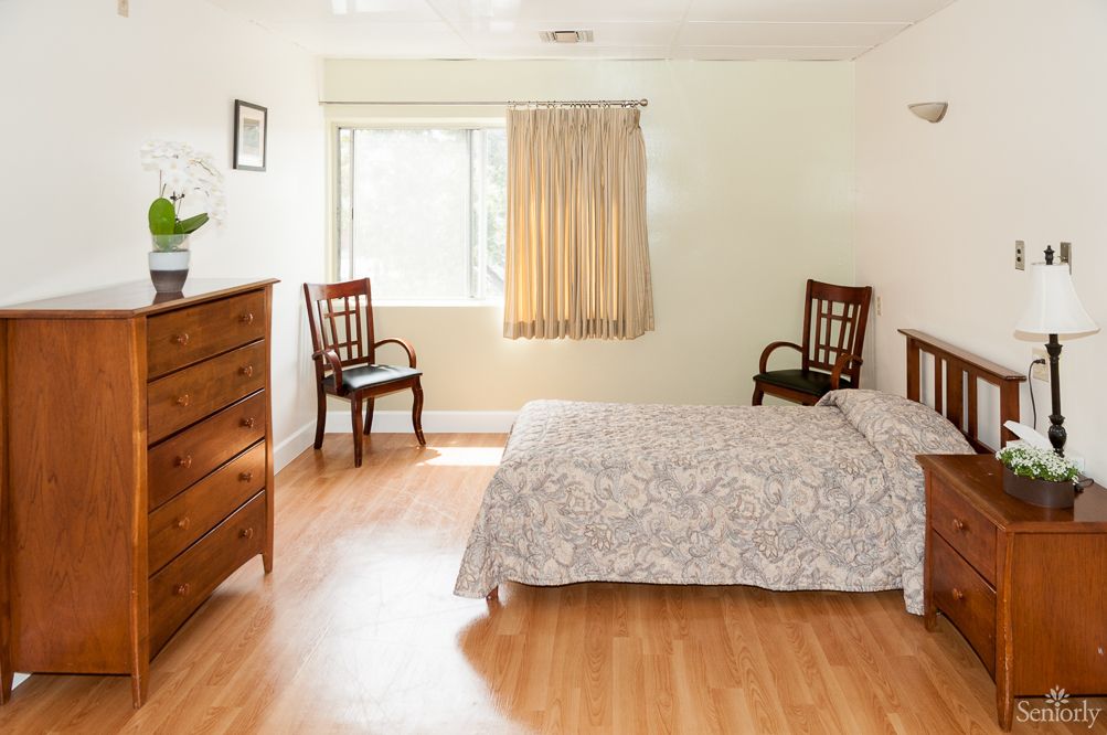 Interior view of a bedroom in Victorian Manor senior living community featuring hardwood flooring and furniture.