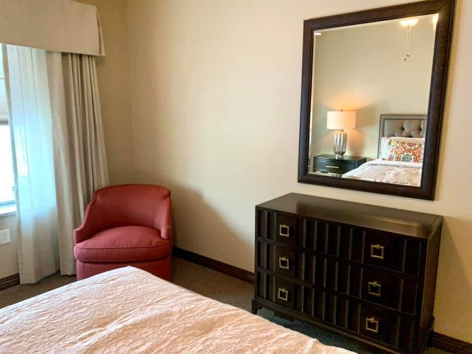 Senior living bedroom interior at Springhouse Village East with bed, chair, and cabinet.