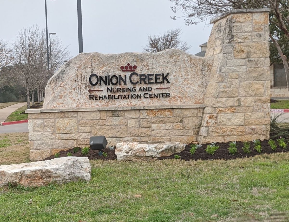 Grassy outdoor park at Senior Care of Onion Creek with architectural buildings and natural vegetation.