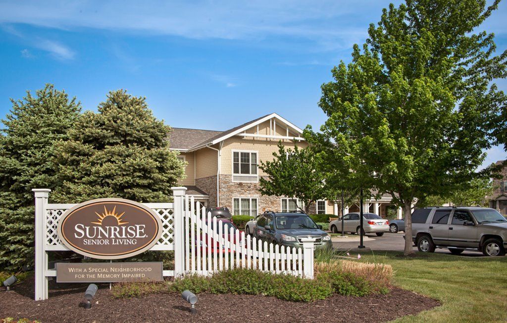 Senior residents enjoying outdoors at Sunrise Assisted Living in Overland Park with cars and picket fence.