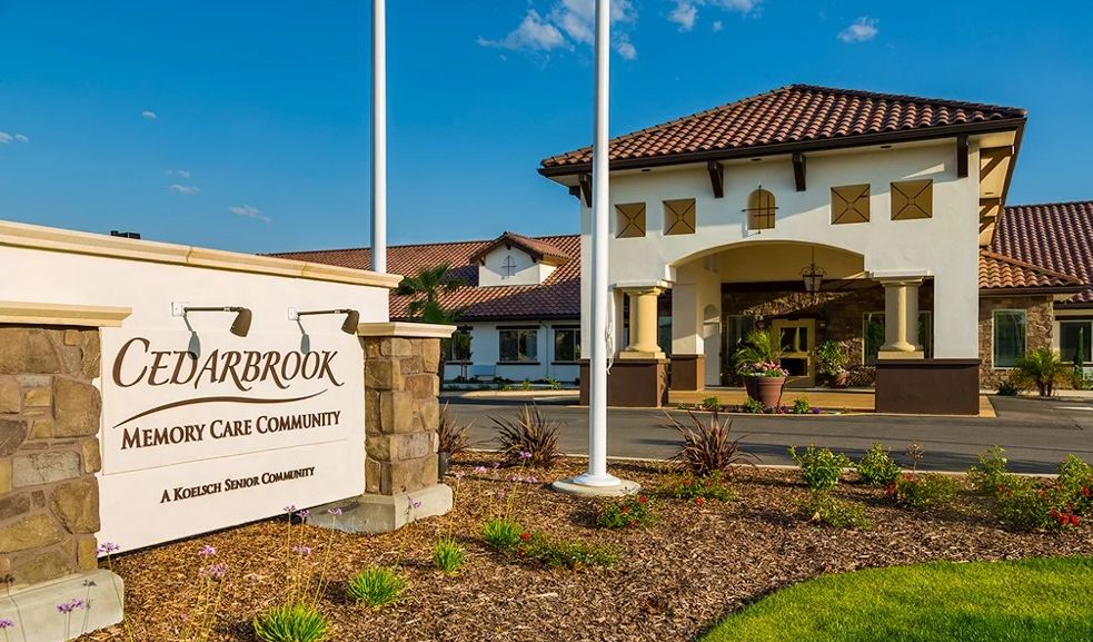 Architectural view of Cedarbrook senior living community featuring villa-style housing, resort amenities, and lush outdoor plants.