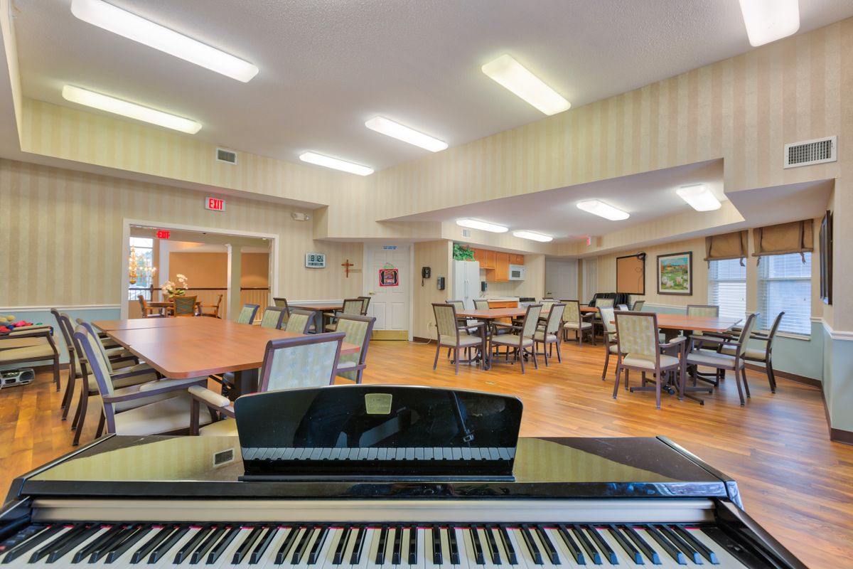 Senior living community interior with hardwood floors, grand piano, art paintings, and furniture.