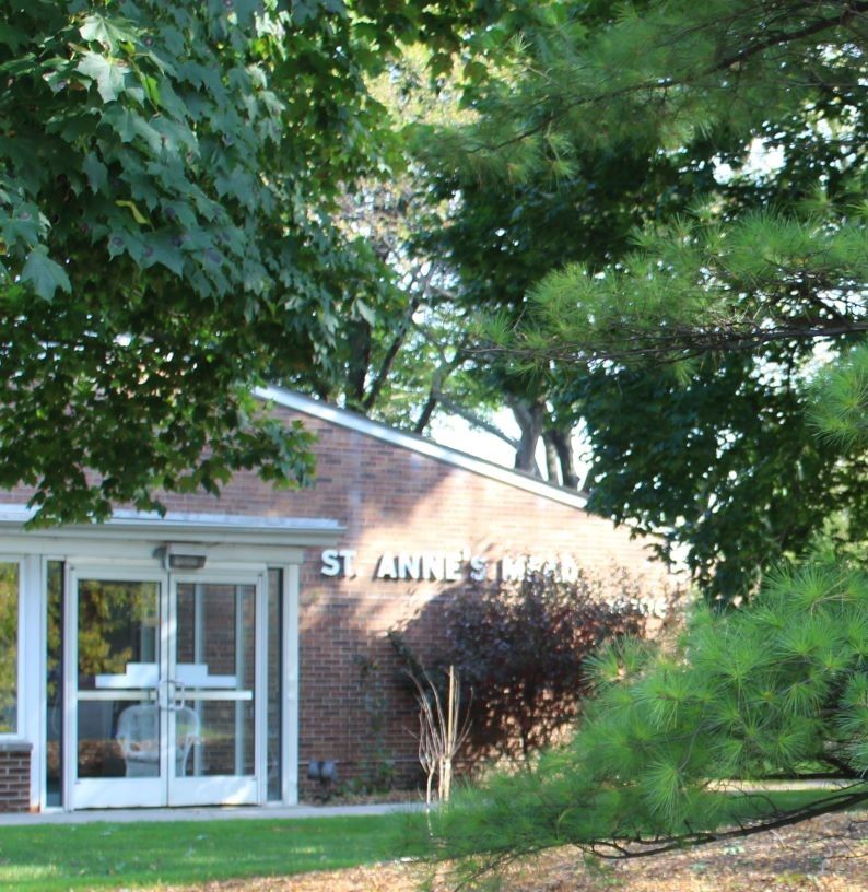 Plant-filled outdoor view of St. Anne's Mead senior living community with brick buildings.
