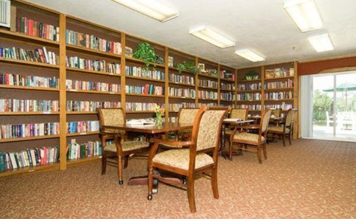 Seniors enjoying a library with books, comfortable furniture, and plants at Villa De Anza Assisted Living.
