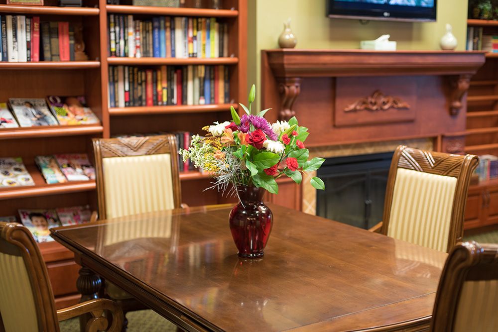 Senior resident enjoying a book in the living room of Garden Plaza of Florissant, surrounded by flowers.