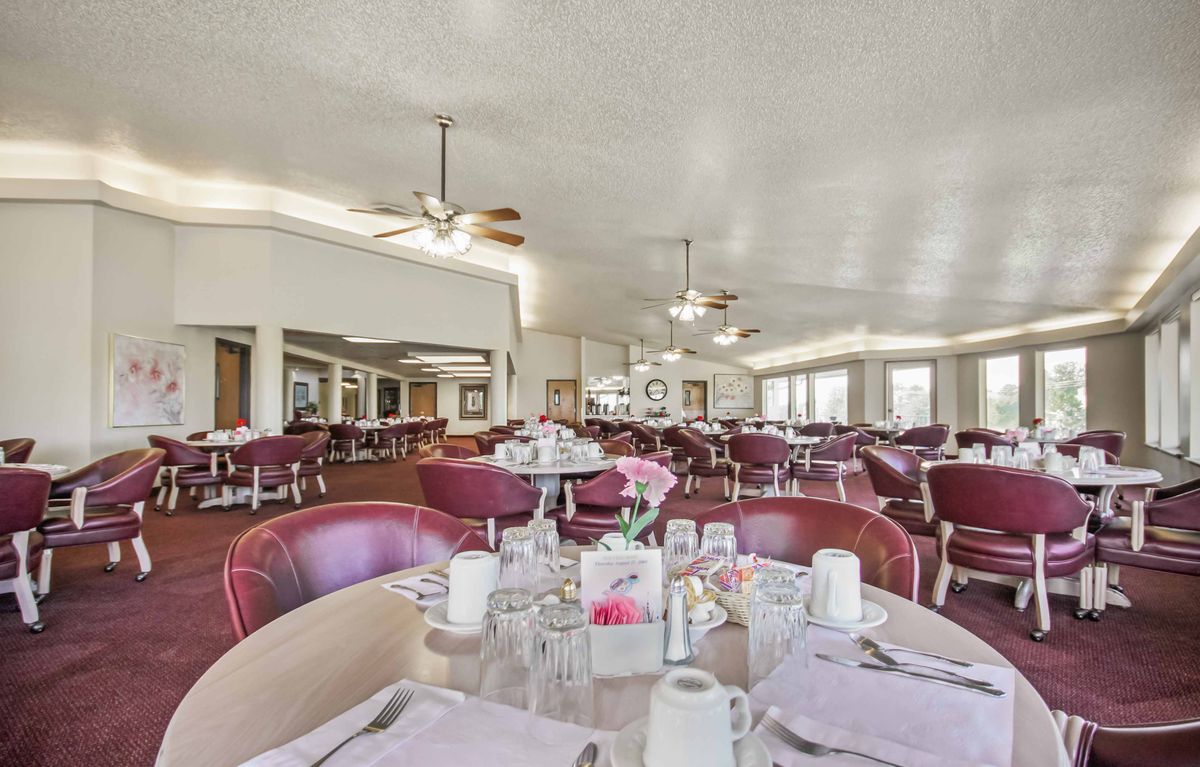 Senior living community dining hall with tables, chairs, ceiling fan, and cutlery.