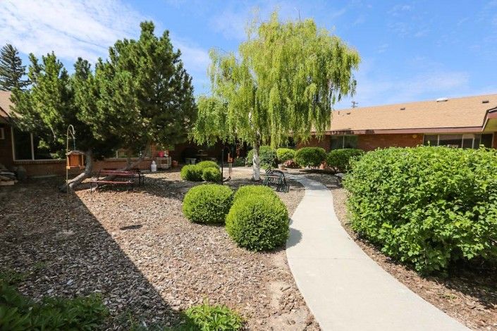 Heritage Assisted Living of Twin Falls, a villa with lush gardens, park benches, and woodland paths.