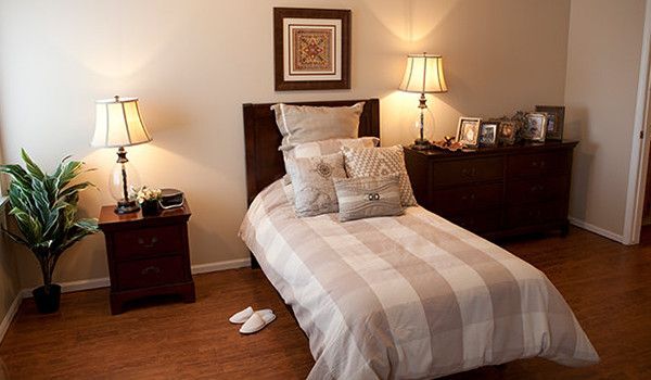 Senior living bedroom at The Village At Primacy Place with bed, table lamp, and home decor.