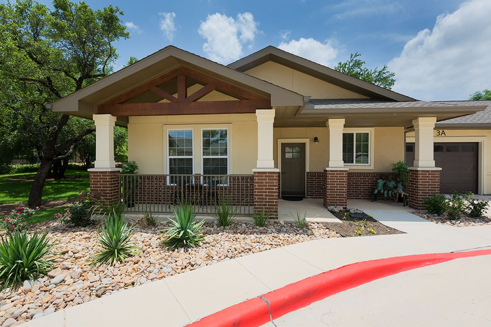 Architectural view of The Enclave at Cedar Park Senior Living community with lush greenery.