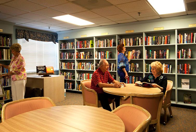 Senior residents at Coral Oaks enjoying a book in the library and dining area.
