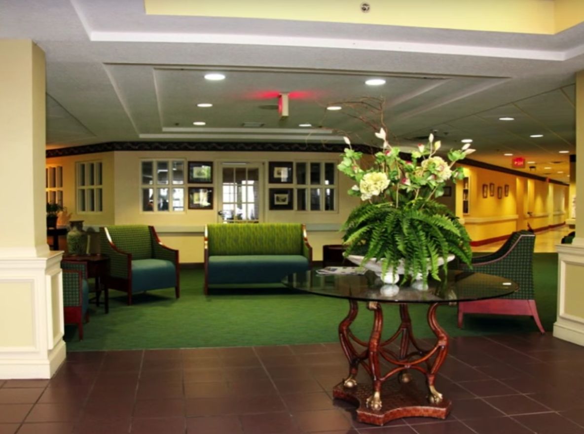 Architectural view of BayView Assisted Living's foyer featuring indoor plants, furniture, and floral arrangements.