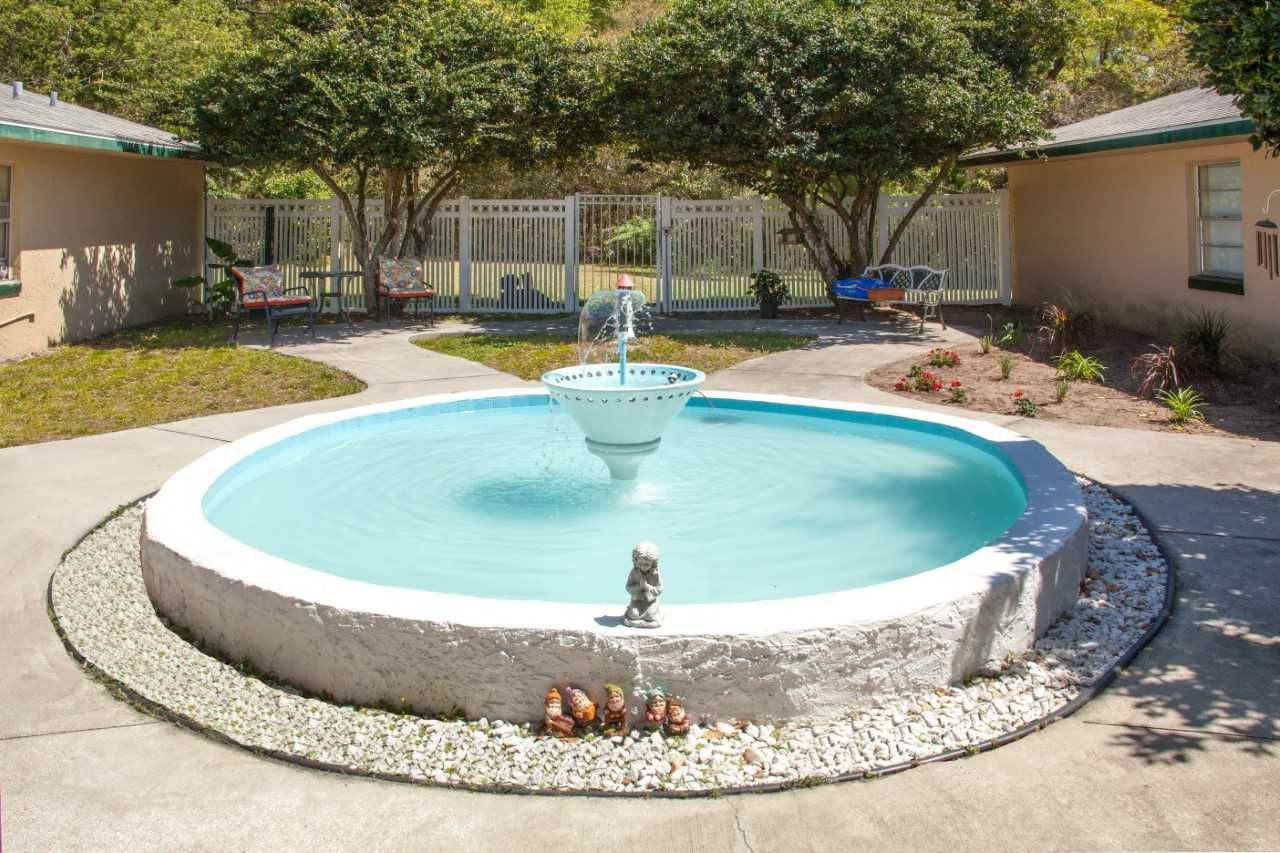 Senior enjoying outdoors at Pleasant Grove Manor with pool, hot tub, and lush greenery.