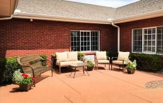 Senior living community Courtyard Village of Kewanee featuring outdoor patio, lush greenery, and cozy furniture.