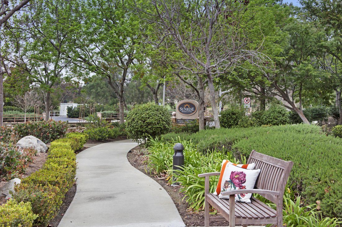 Senior living community, Sunrise of Mission Viejo, featuring lush gardens, park benches, and scenic walkways.