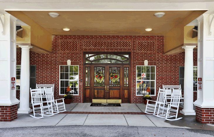 Senior living community, Sodalis Tampa, featuring a porch with rocking chairs and lush plants.