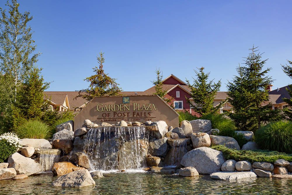 Scenic view of the Bridge at Post Falls senior living community, featuring lush vegetation, pond, and architecture.