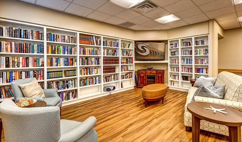 Senior residents enjoying a library with bookcases, chairs, and couch at Sentara Village, Virginia Beach.