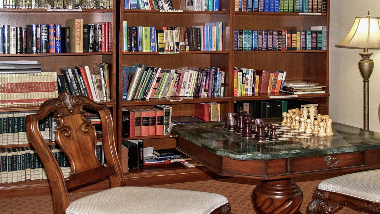 Senior living community library at Rocky Ridge with bookcases, chairs, and tables indoors.