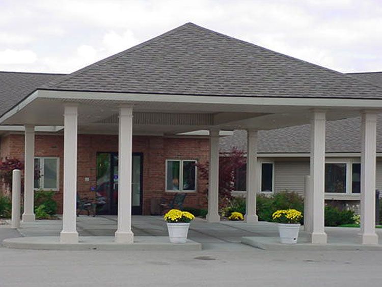 Grand Pines Assisted Living Center exterior featuring a portico, porch, and lush plants.