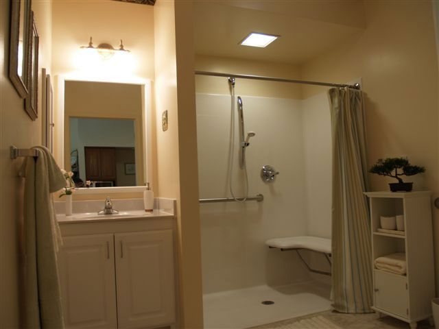 Interior view of a bathroom with a shower and plant decor at Corner Room, Grand Pines Assisted Living Center.