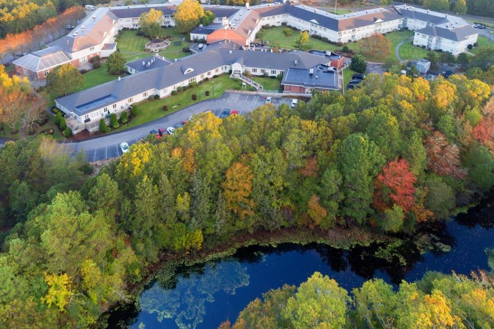 Aerial view of Maplewood at Mayflower Place senior living community with lush vegetation and lake.