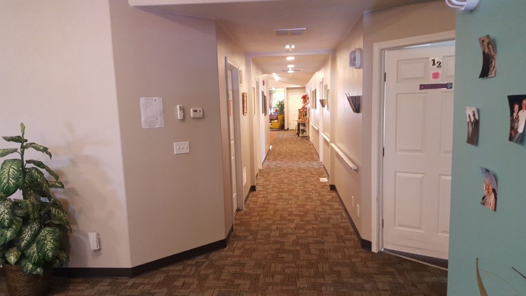 Senior resident walking in the well-lit hallway of Country Time Assisted Living facility.