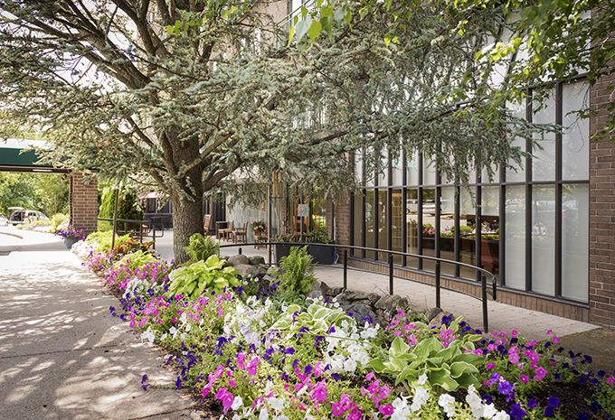 Senior living community at AVIVA Country Club Heights featuring garden paths, geranium plants, and patio furniture.