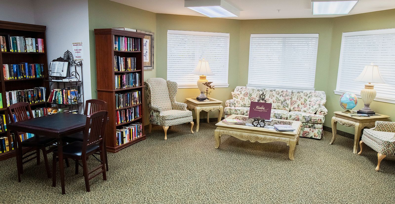 Interior view of Manor at Steeplechase senior living community featuring a cozy living room with bookcase and furniture.