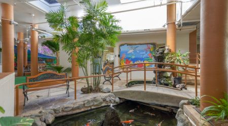 Senior living community, Hale Nani Rehabilitation & Nursing Center, featuring a garden, pond, and outdoor seating.