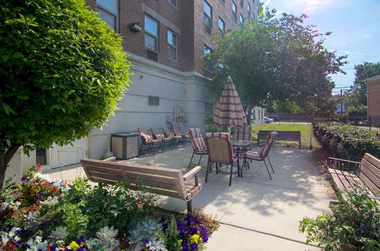 Senior Suites Belmont Cragin's backyard with garden, grass, city view, and patio furniture.